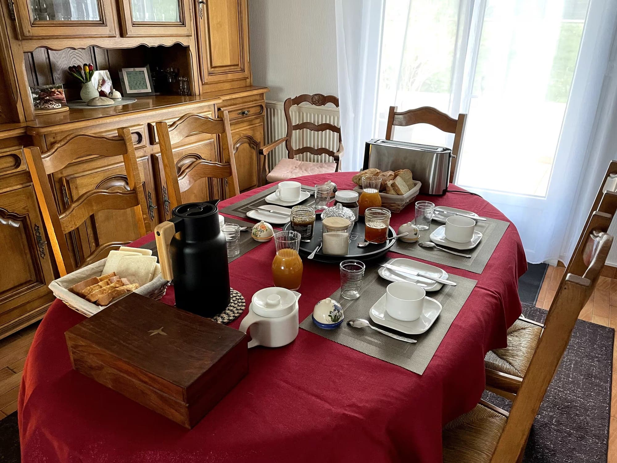 La table du petit-déjeuner dressée sur une nappe rouge devant le buffet en chêne