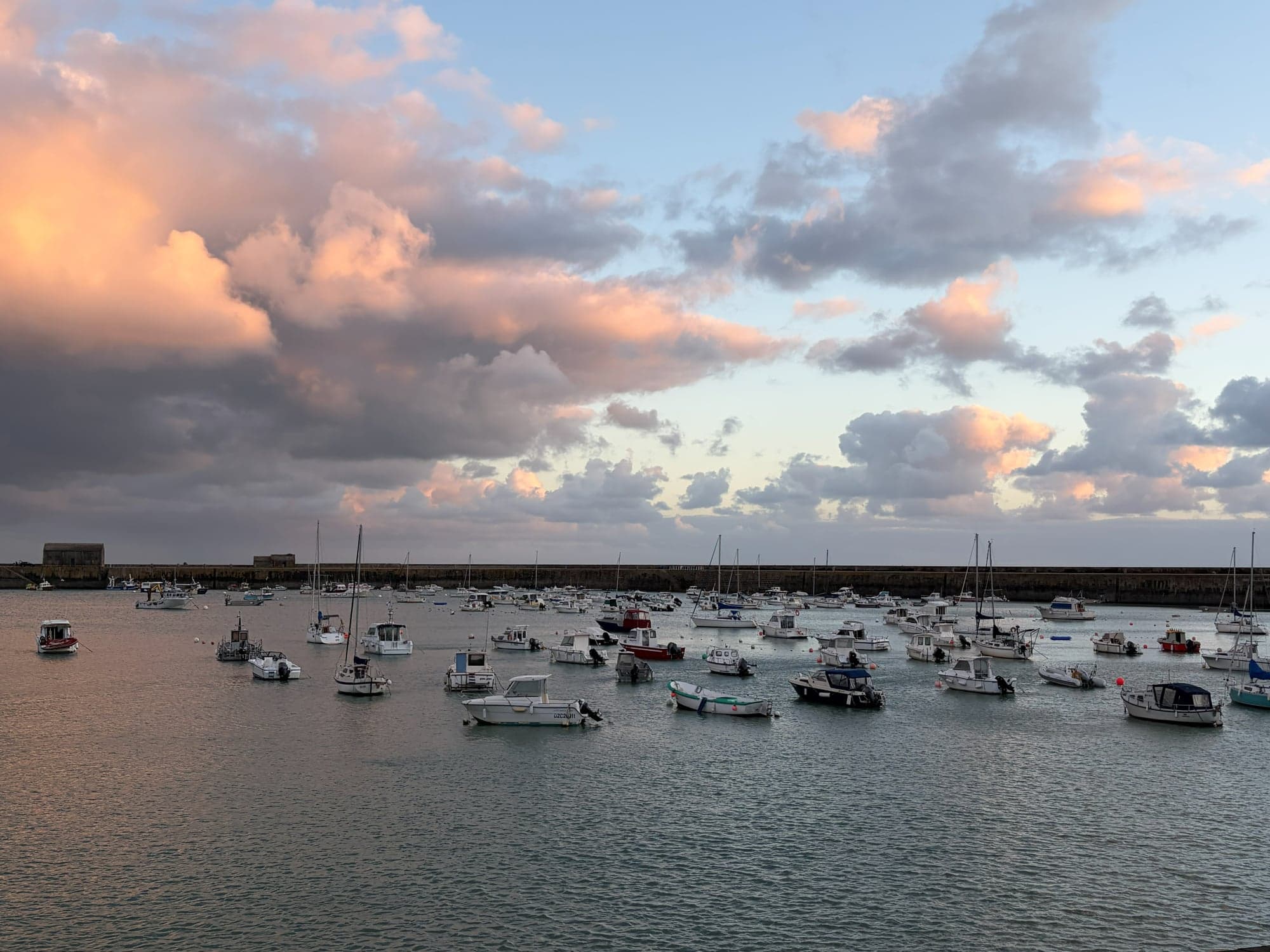 Le port de Granville au crépuscule : bateaux de pêche au mouillage devant la grande jetée, nuages roses sur la mer